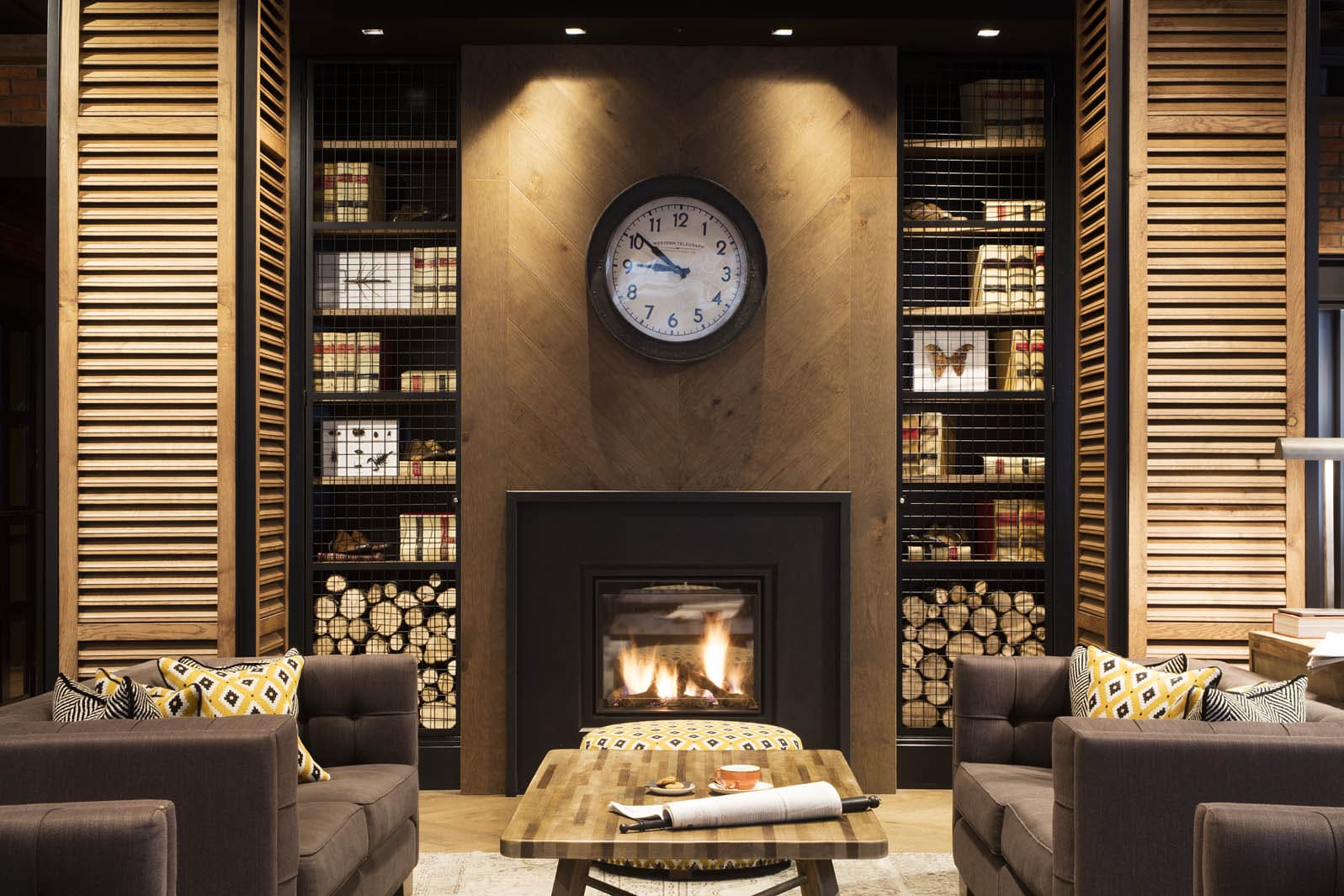 Se observa una zona de estar con chimenea, sillones y estanterías de libros detrás.