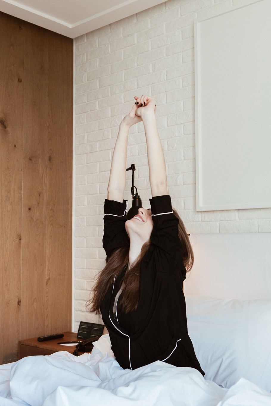Una persona estira las sábanas sobre una cama en una habitación con pared blanca y suelo de madera.