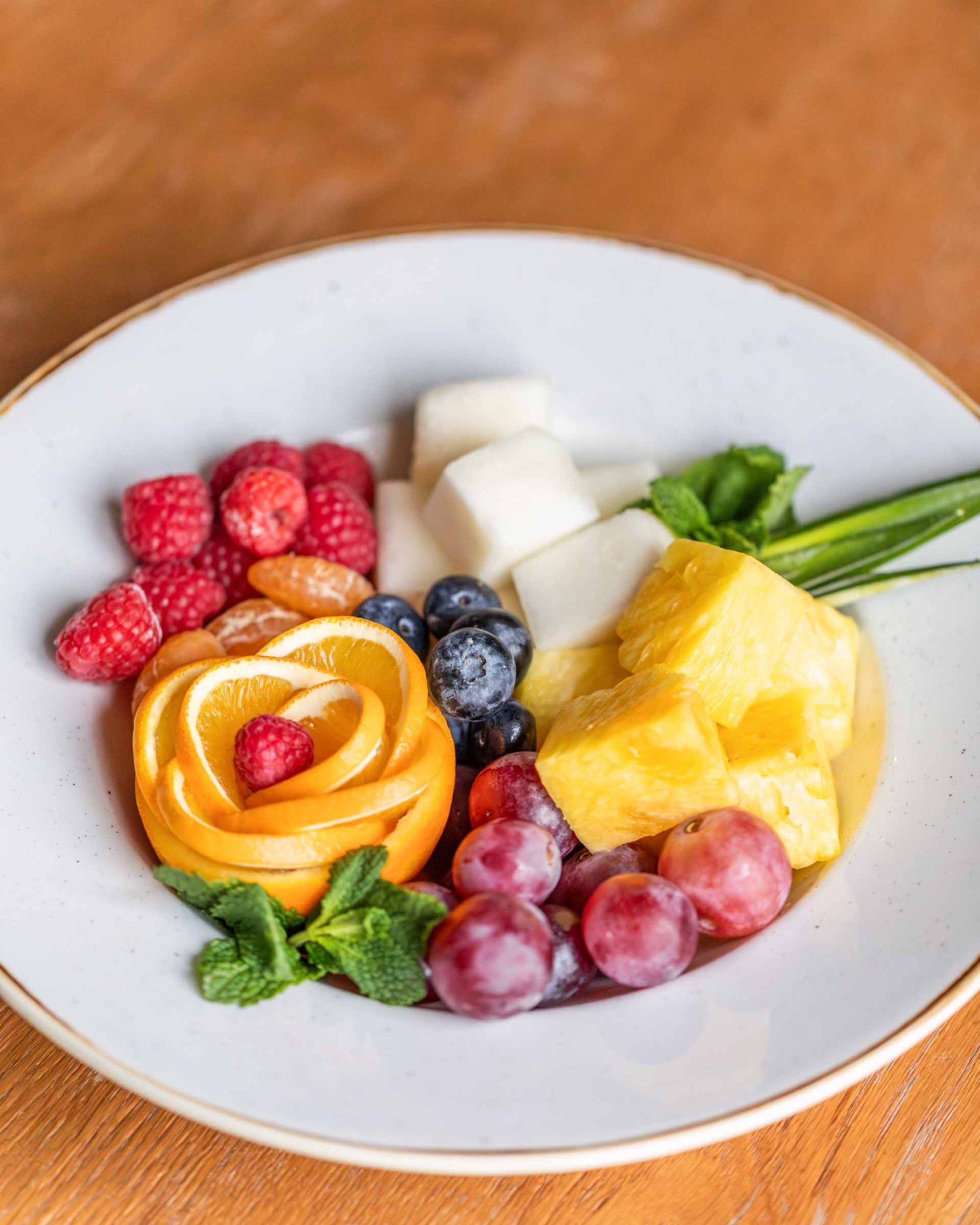 Describe un plato con fruta variada, incluida fresa, uvas, queso y rodajas de naranja.
