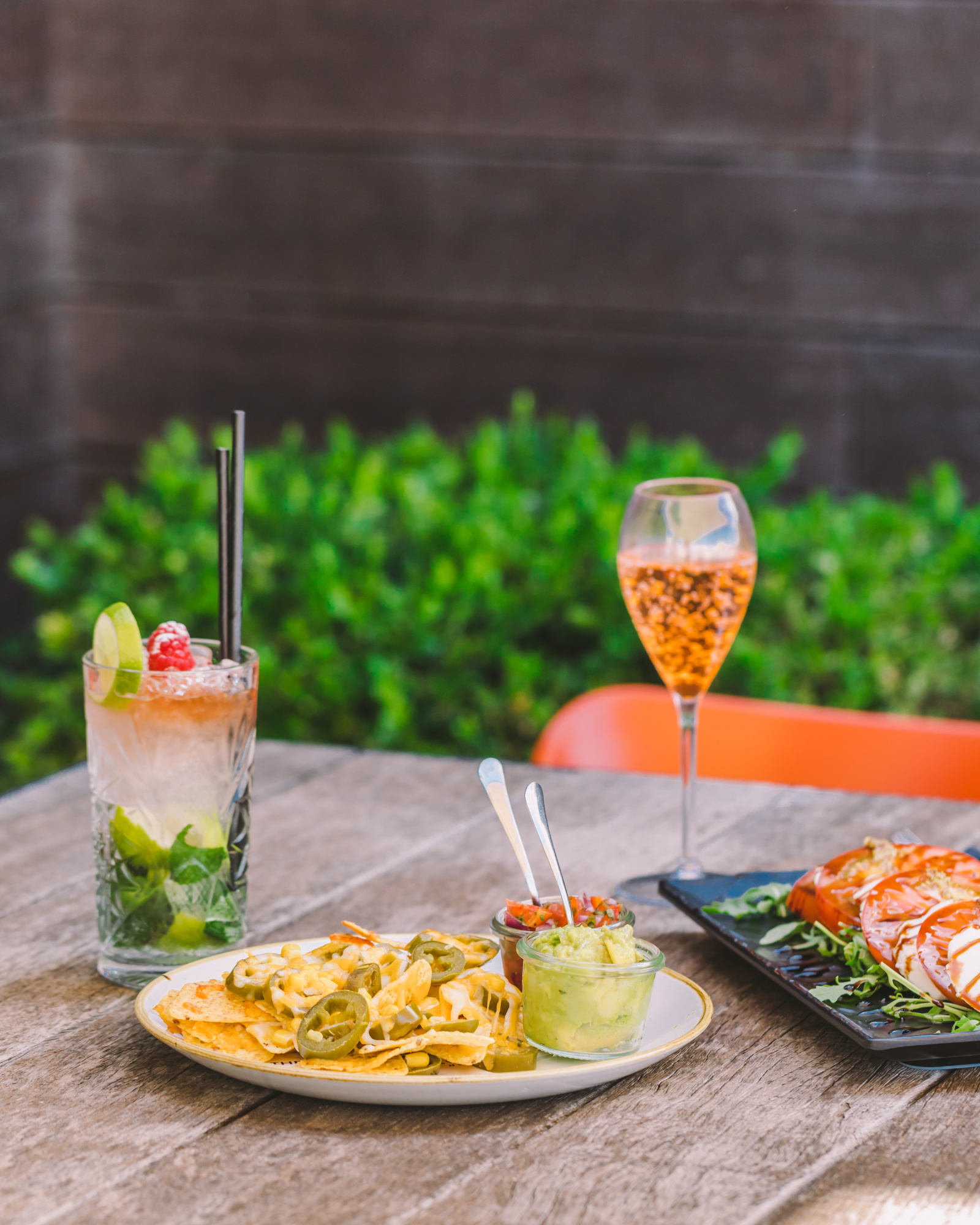 Se ven tres cócteles en vasos junto a platos de comida sobre una mesa al aire libre.
