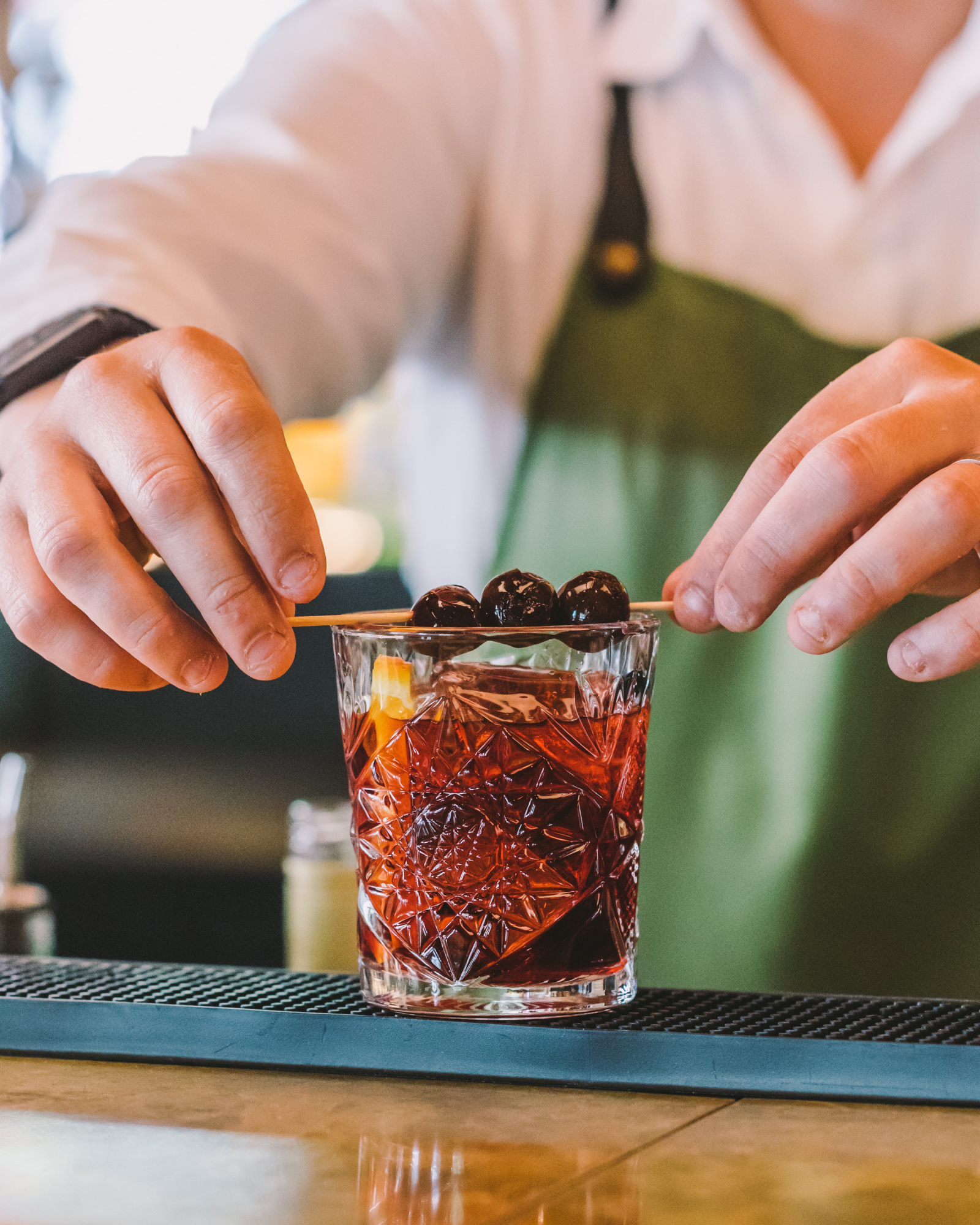 Una persona prepara un cóctel en un vaso con hielo sobre una mesa de bar.