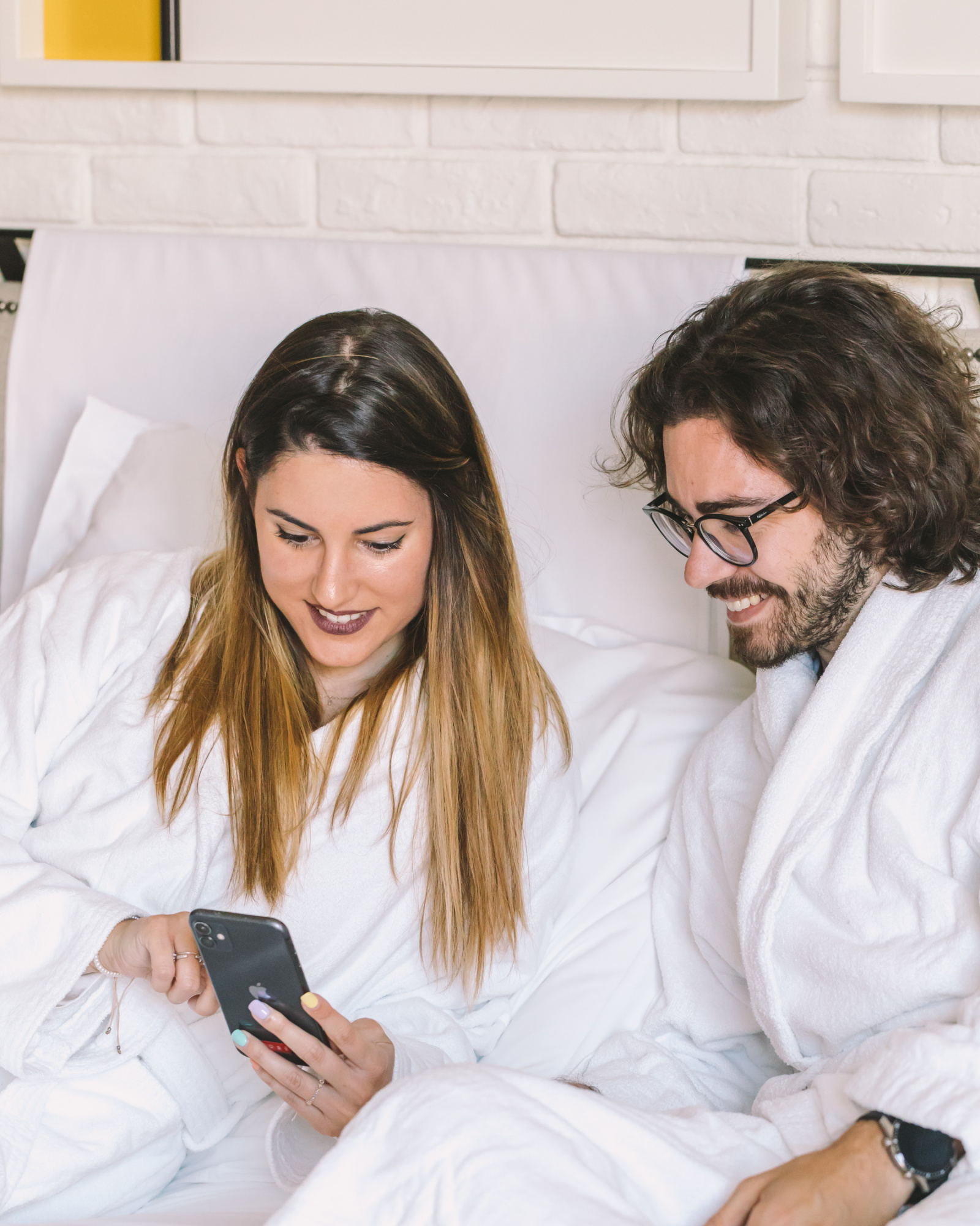 Una pareja descansa en una cama con ropa de dormir y mira sus teléfonos.