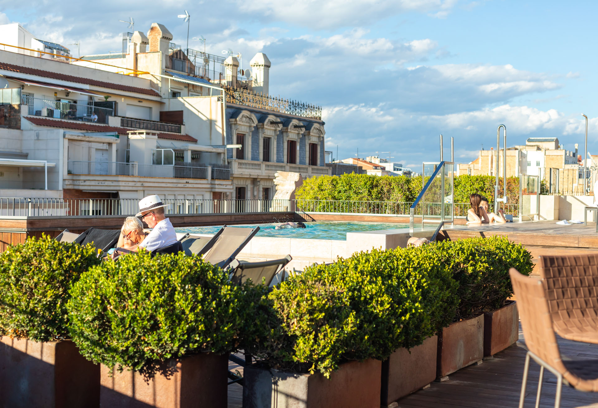 Terraza exterior con piscina al fondo y plantas en maceteros junto a sillones.
