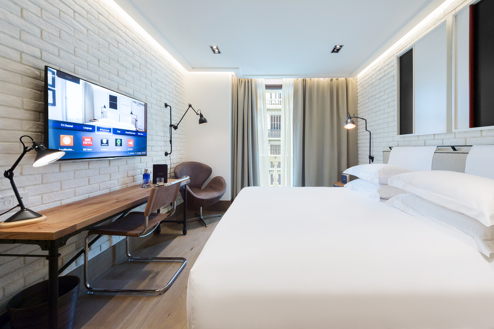 Describe un dormitorio luminoso con cama doble, escritorio y televisión de pantalla plana.