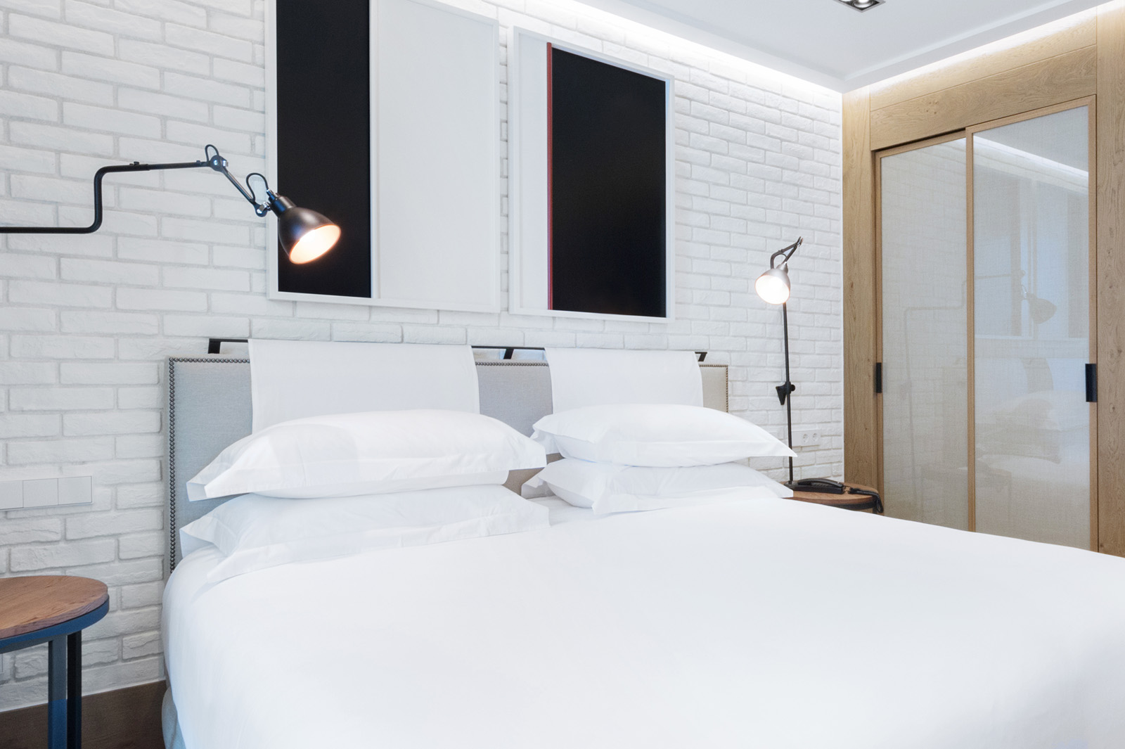 Se ve una cama con ropa de cama blanca, cabecero acolchado y lámparas de pared en una habitación moderna.