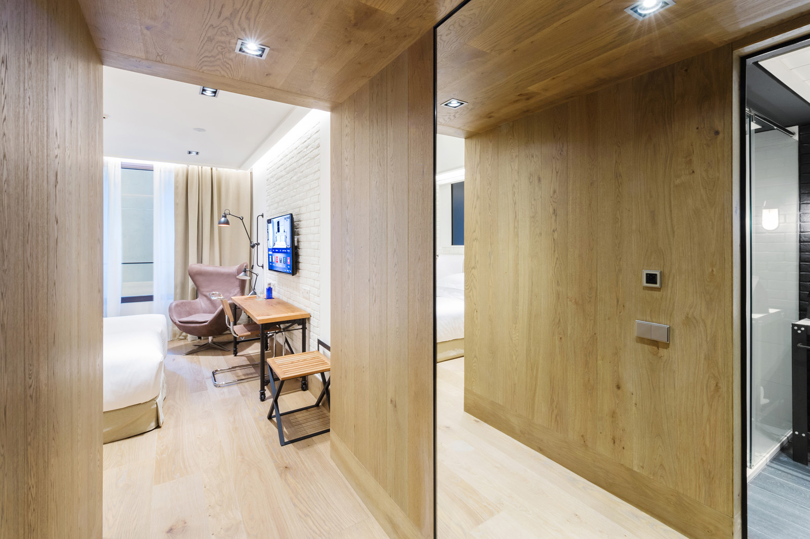 Se ve un pasillo con suelo claro, una puerta de acceso al fondo y un escritorio con silla junto a una ventana.