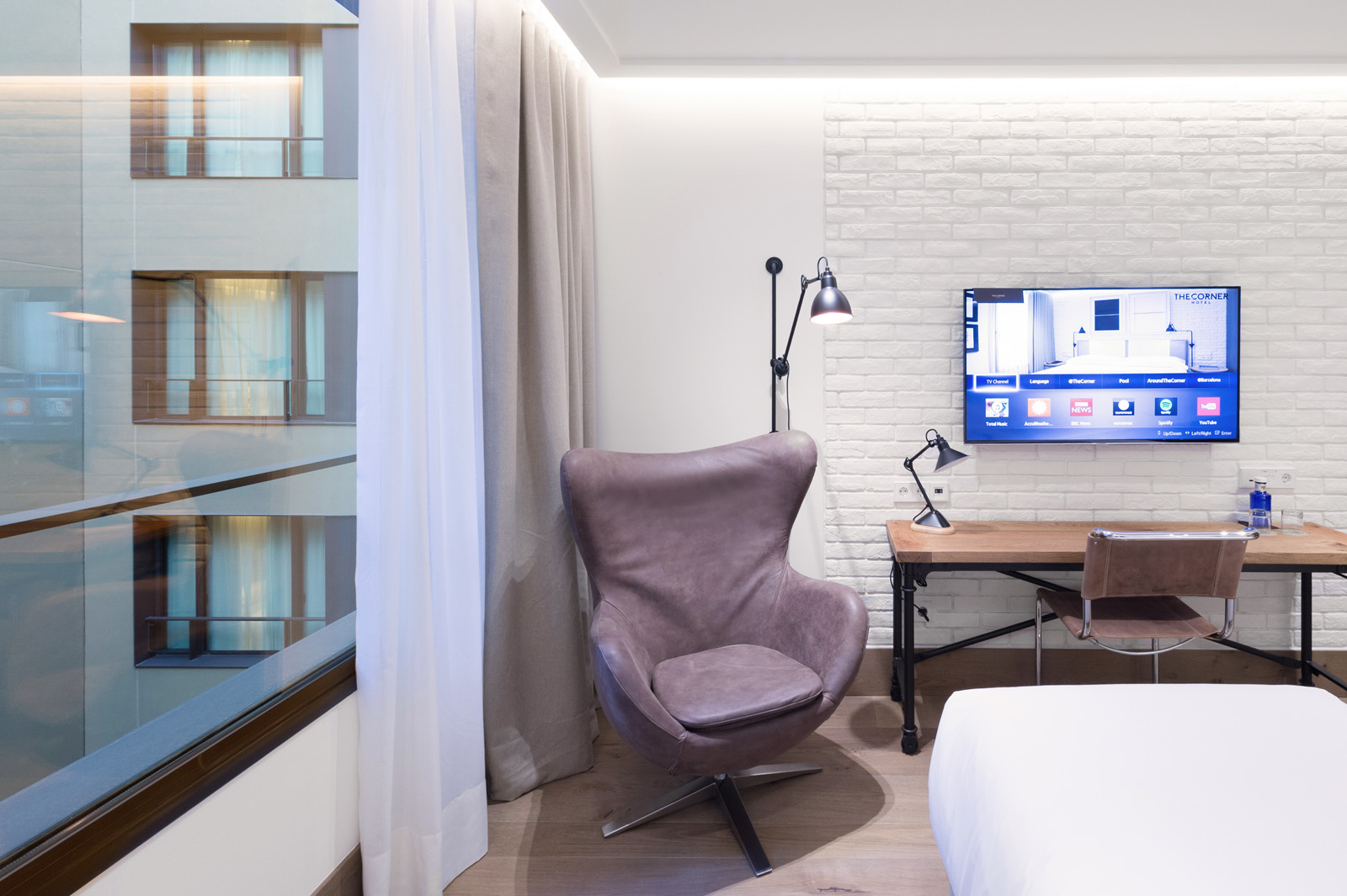 Espacio de estudio con silla acolchada, escritorio y un ventanal con cortinas blancas.