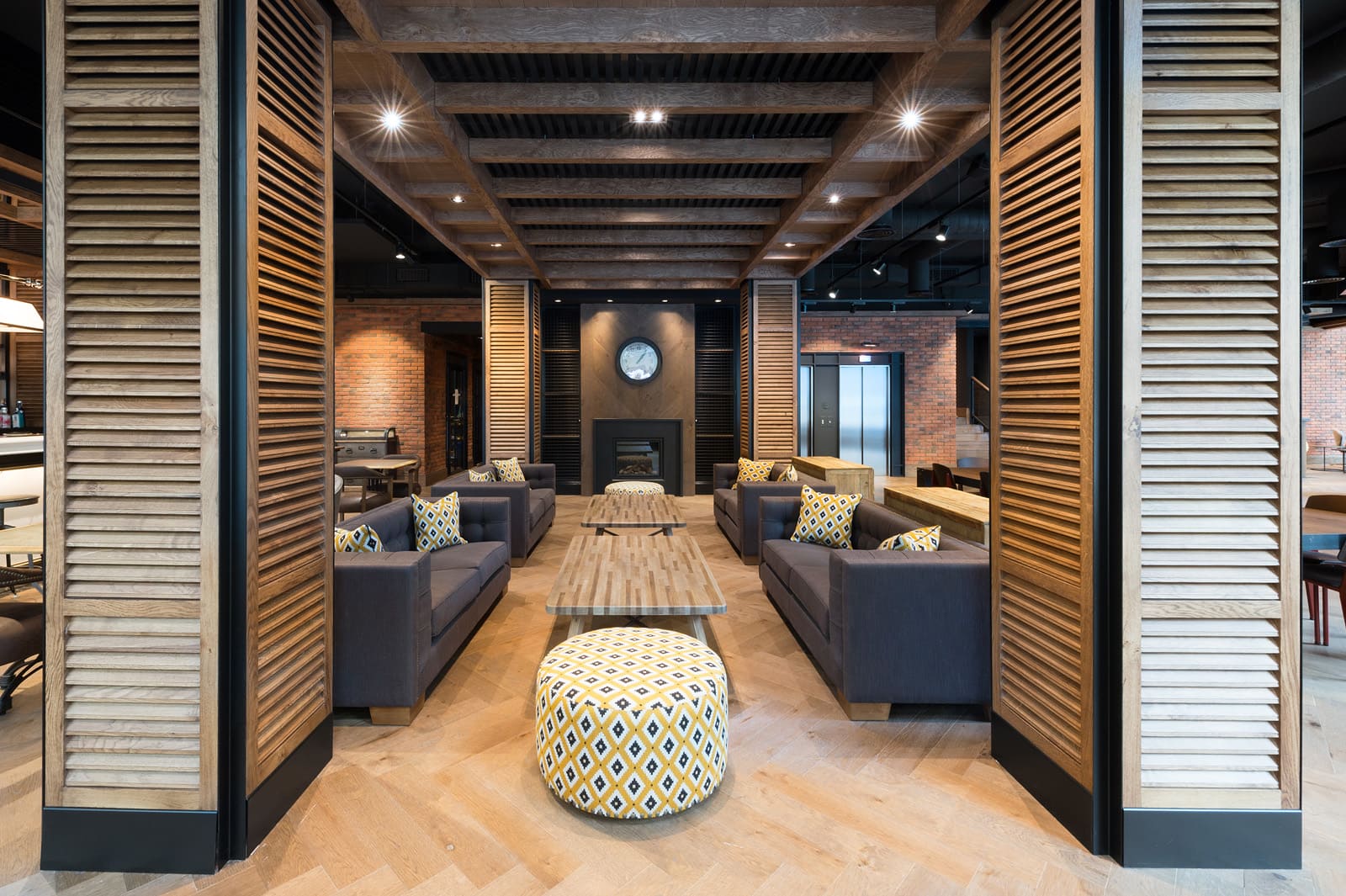Sala de estar con sillones grises, mesa central y una zona de paso entre columnas decorativas.