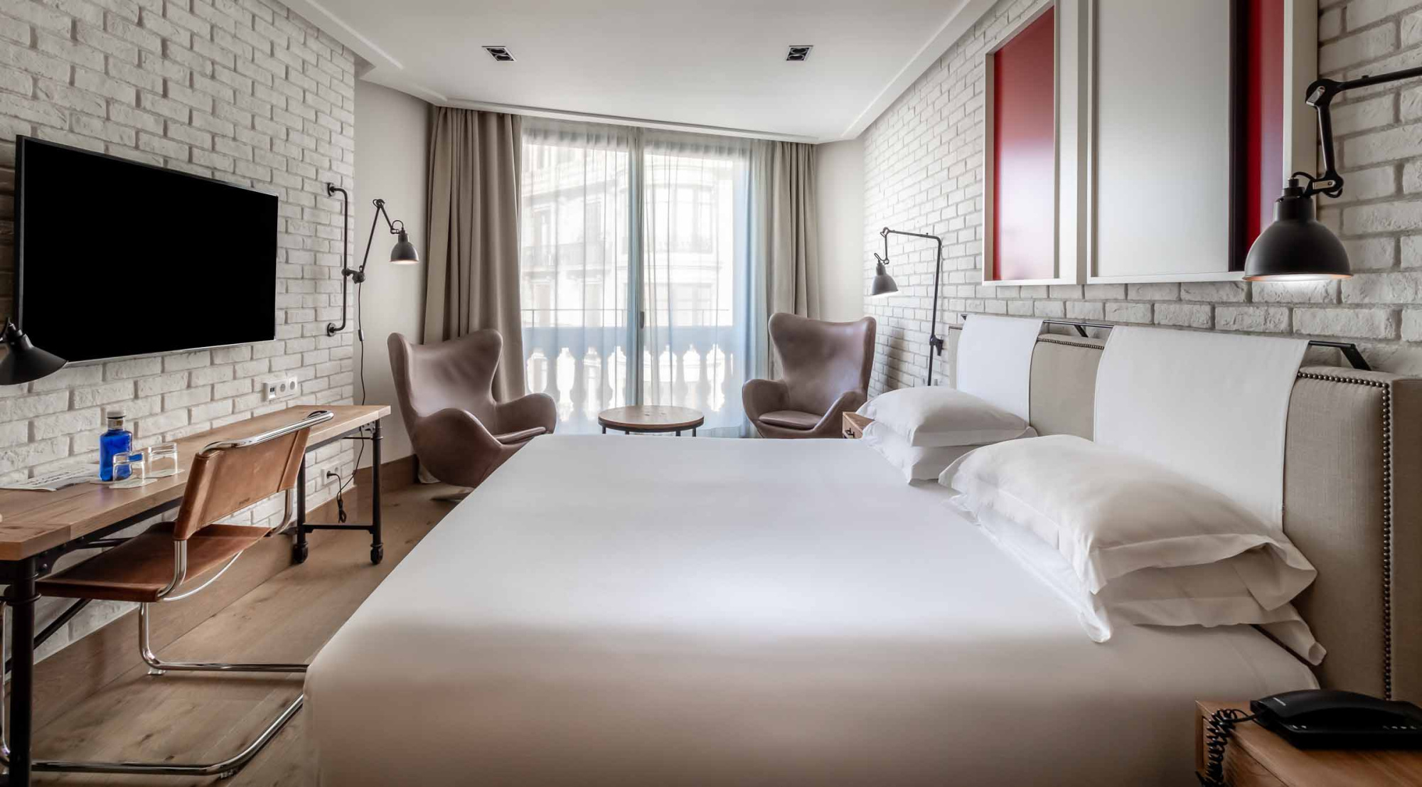 Dormitorio moderno con cama doble, televisor y ventana con cortinas en la pared del fondo.