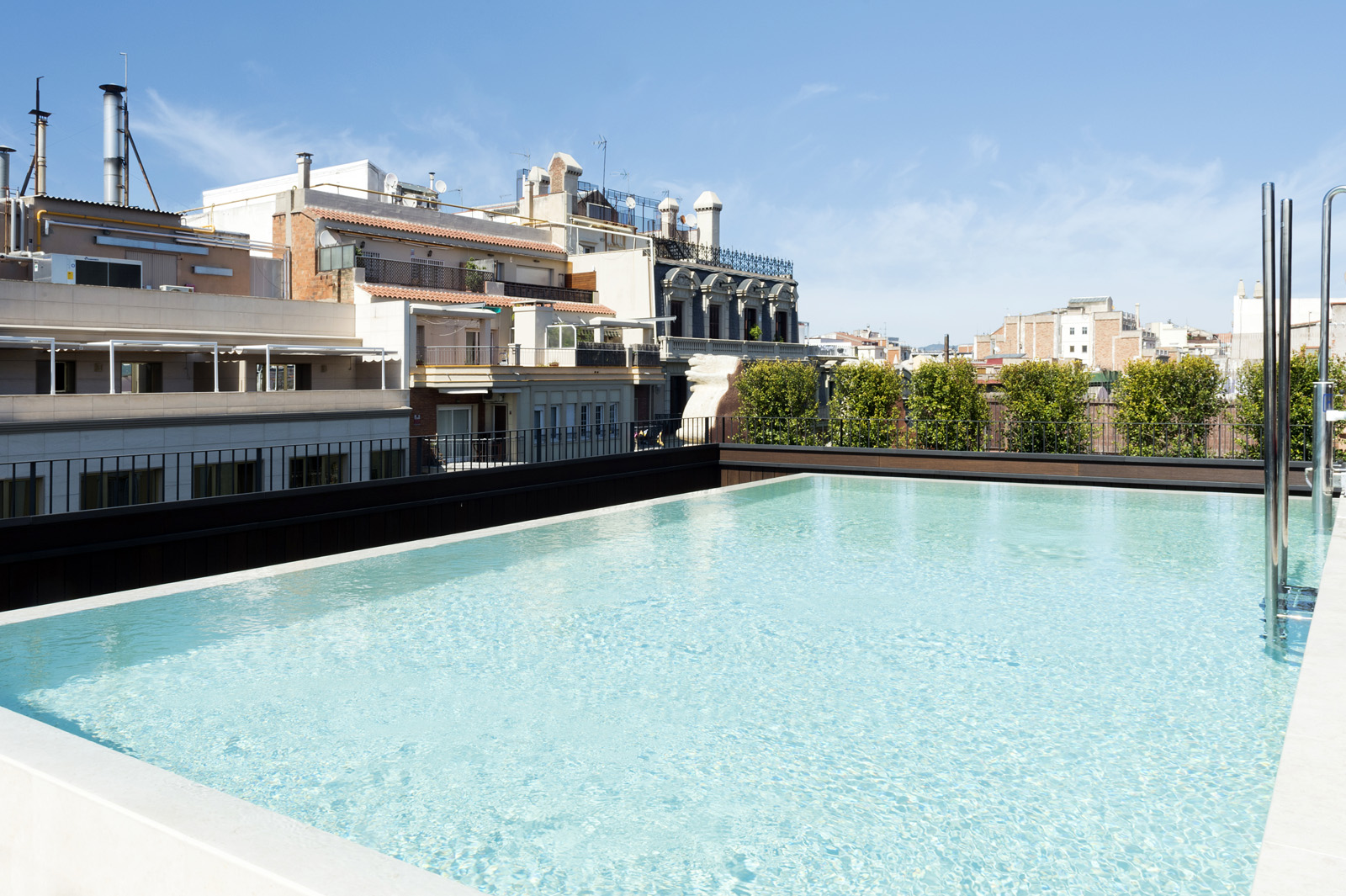 Se ve una piscina exterior con borde claro y agua azul en una terraza al aire libre.