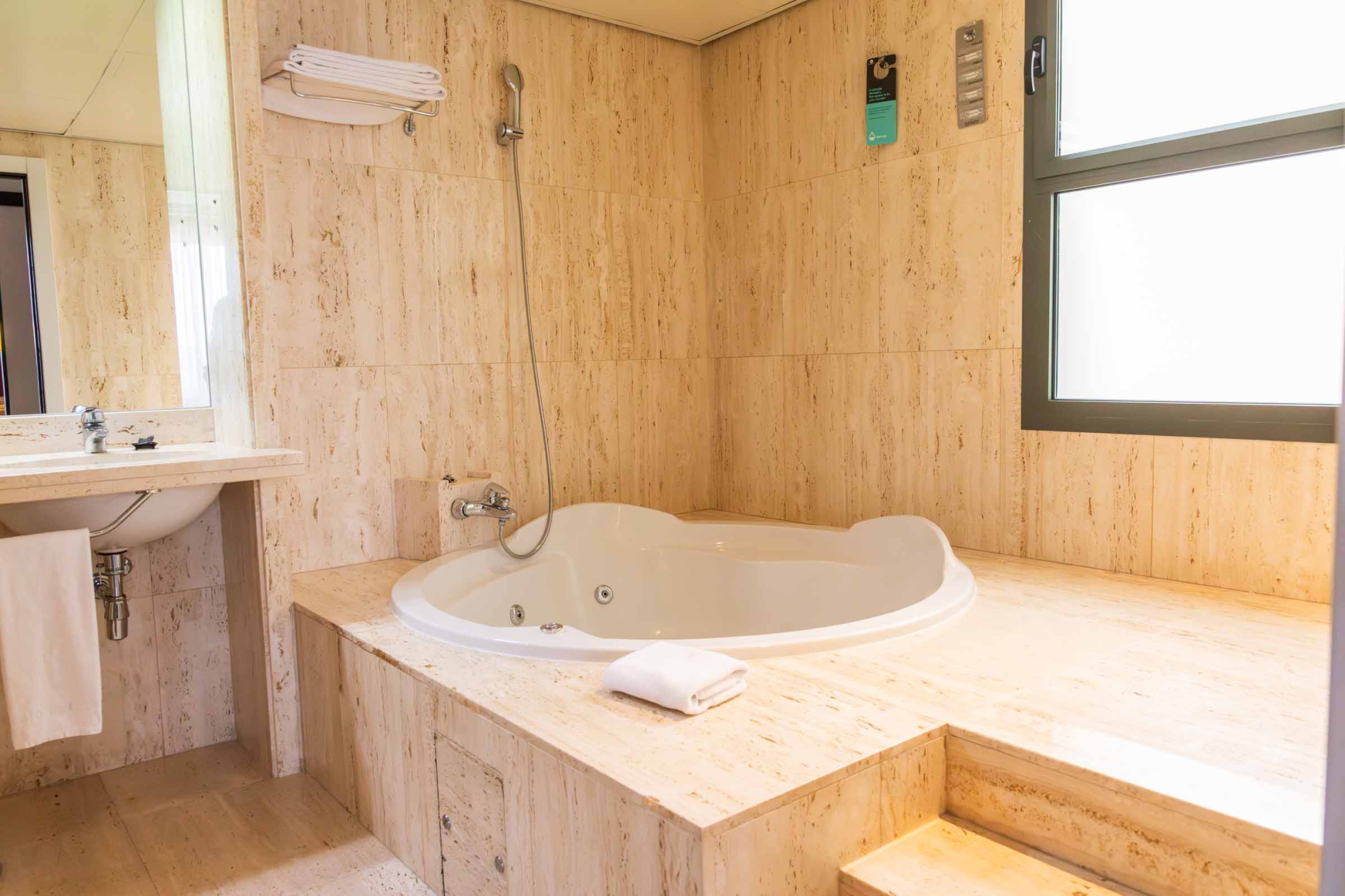 Se ve una bañera ovalada con grifería y una ventana en un baño con paredes de madera clara.