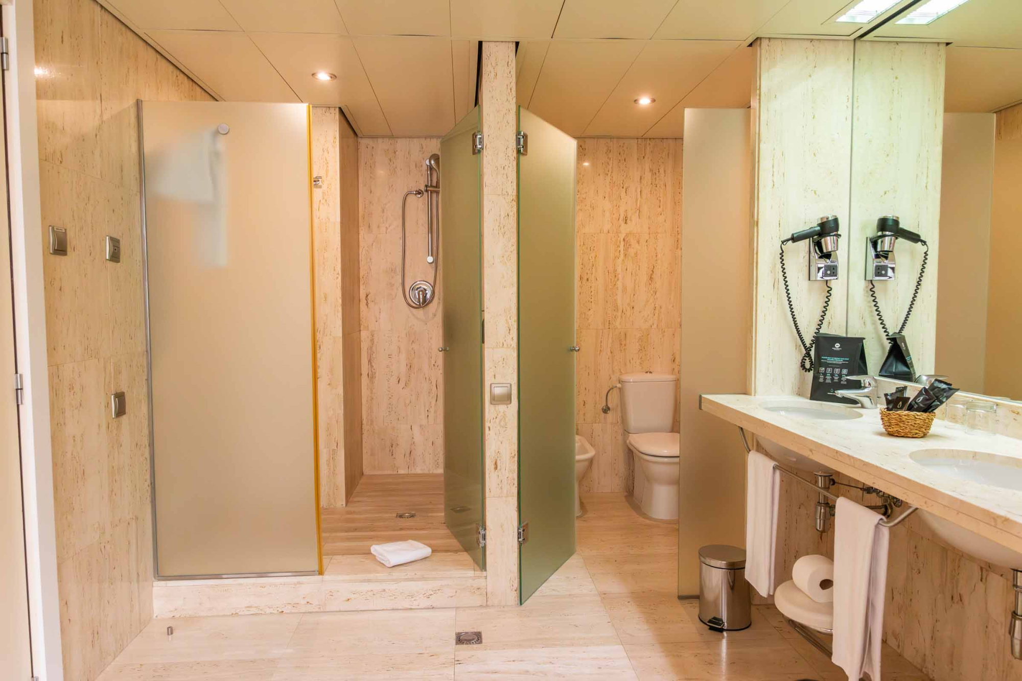 Se ve un baño con mampara de ducha, grifería, lavabo doble y espejo iluminado.