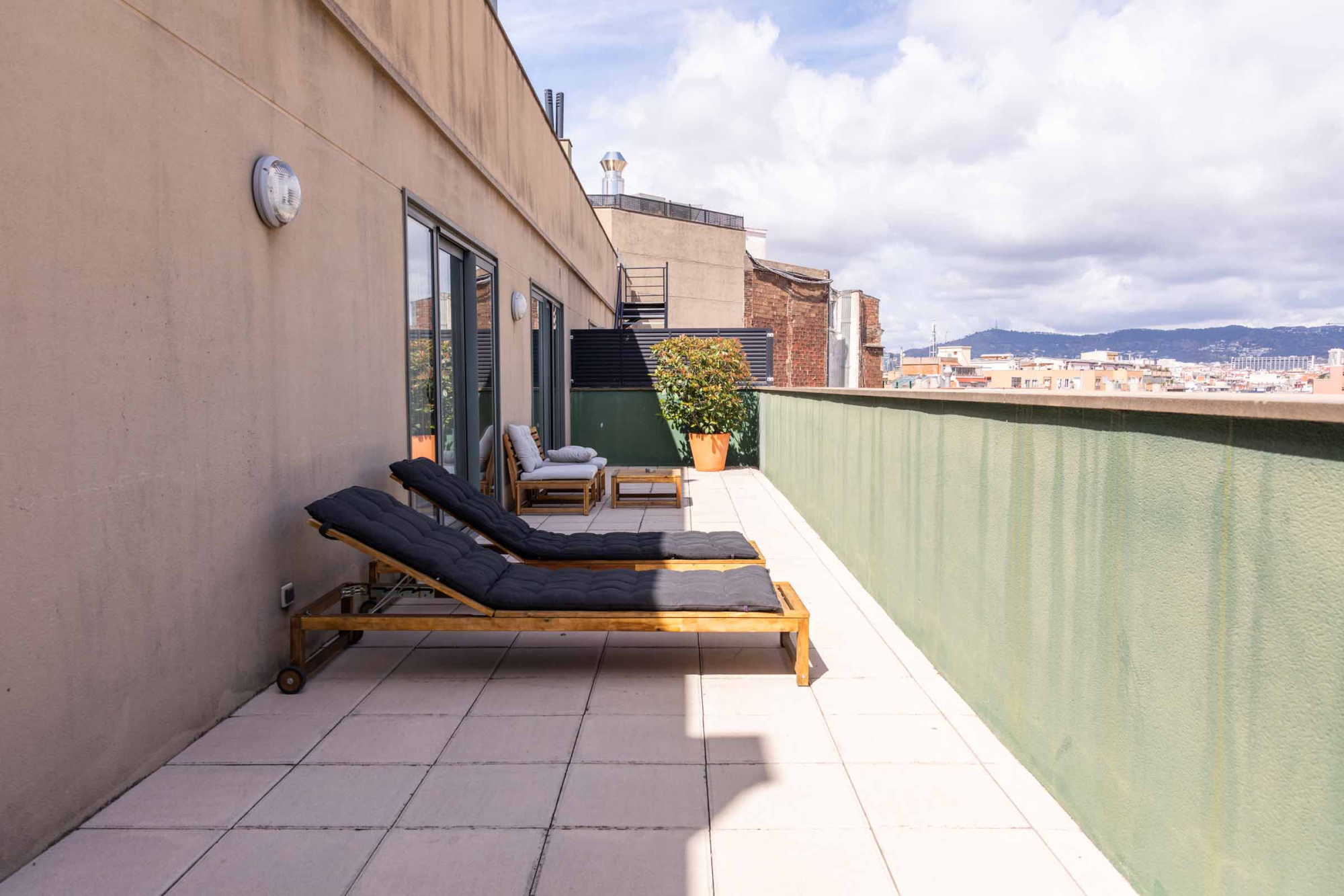 Una terraza exterior con tumbonas y una pared de vidrio junto a una piscina al aire libre.