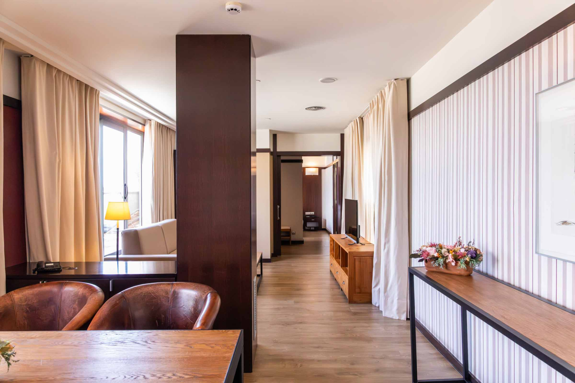 Pasillo interior con sillones de cuero, cortinas claras y muebles en el costado derecho.