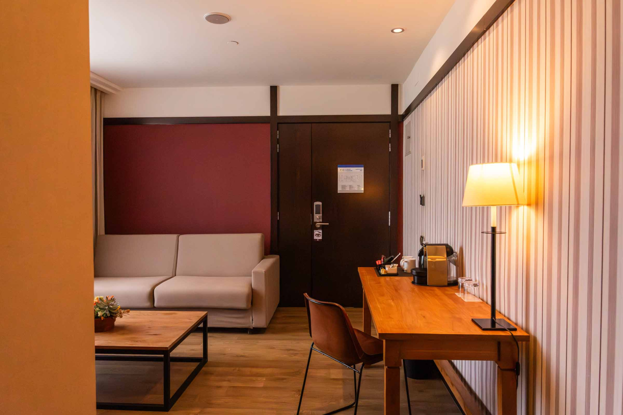 Se ve una sala interior con escritorio, lámpara de pie y un sofá junto a una pared oscura.