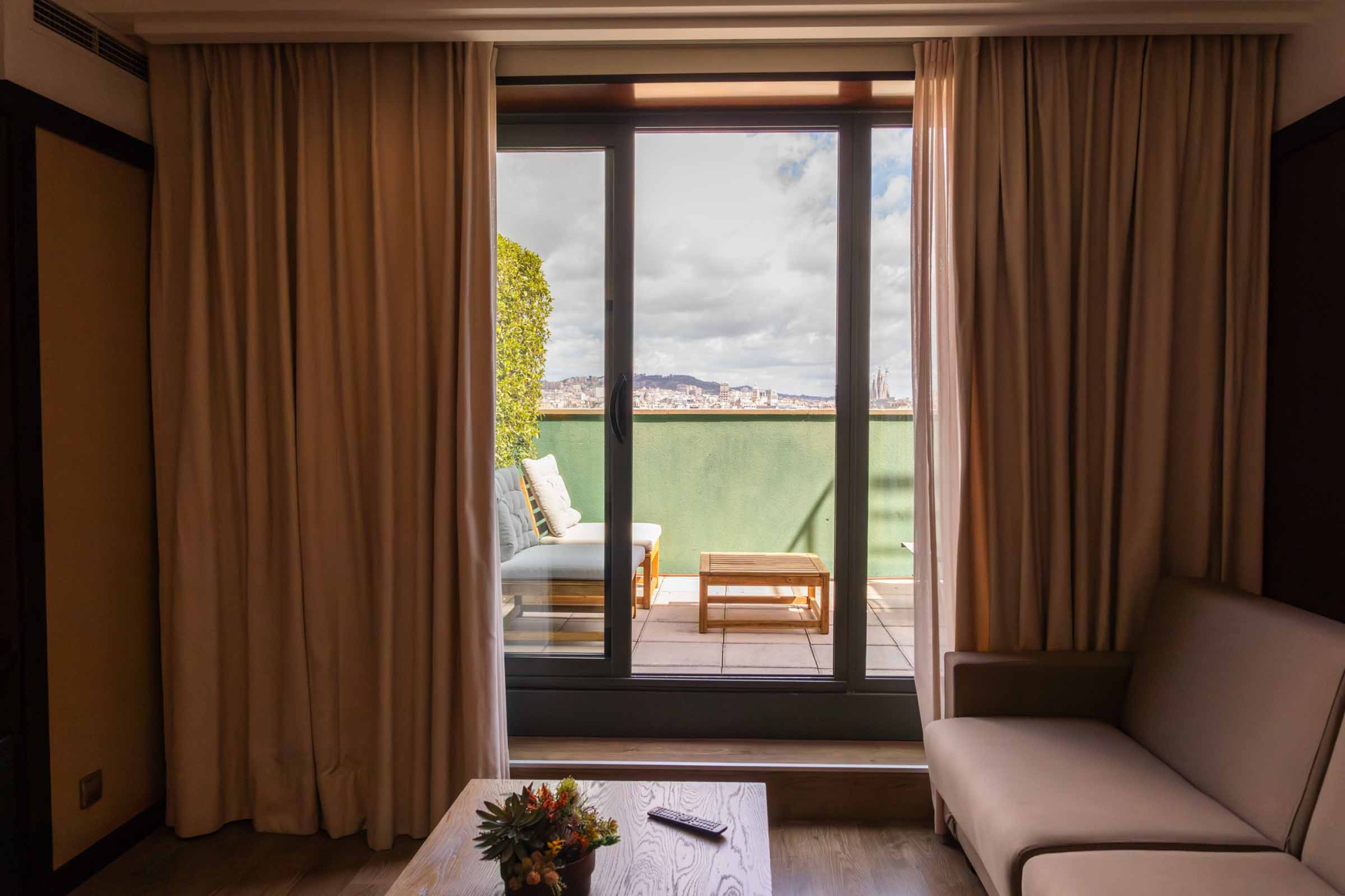 Se ve una sala con sofá y una puerta de vidrio que da acceso a una terraza con barandilla exterior.
