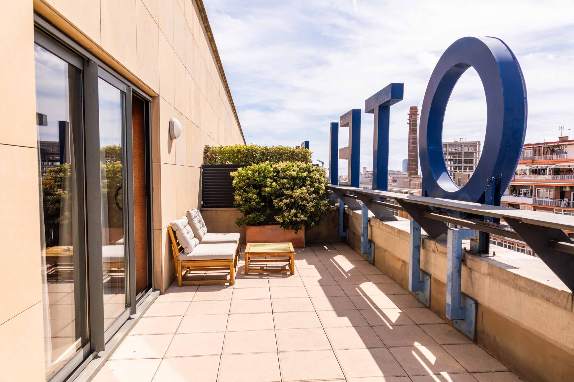 Se ve una terraza con dos tumbonas, una planta decorativa y un gran aro tipo jacuzzi junto a una barandilla con vista urbana.