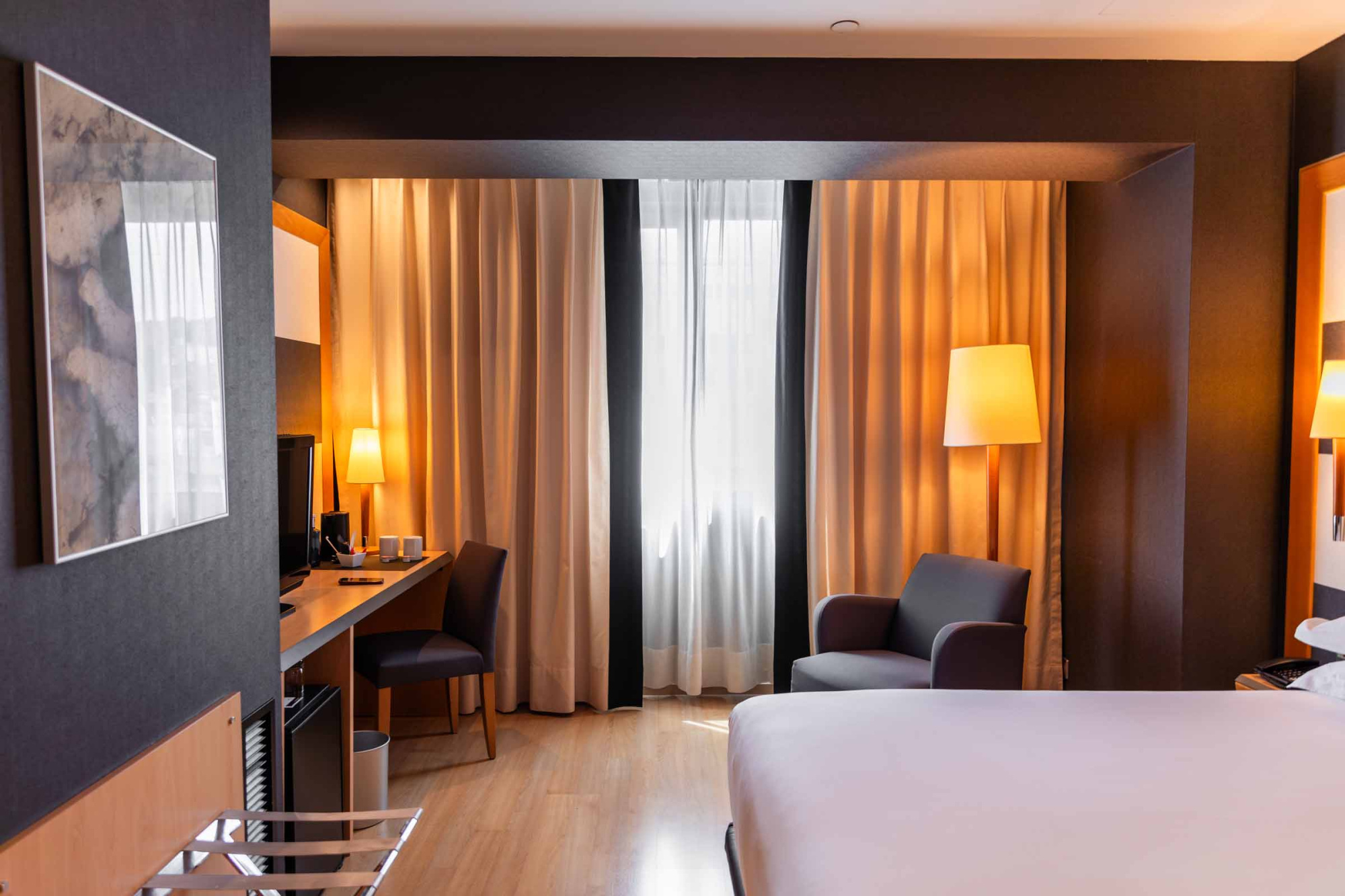 Una habitación luminosa con cama doble, silla y cortinas con luz natural.