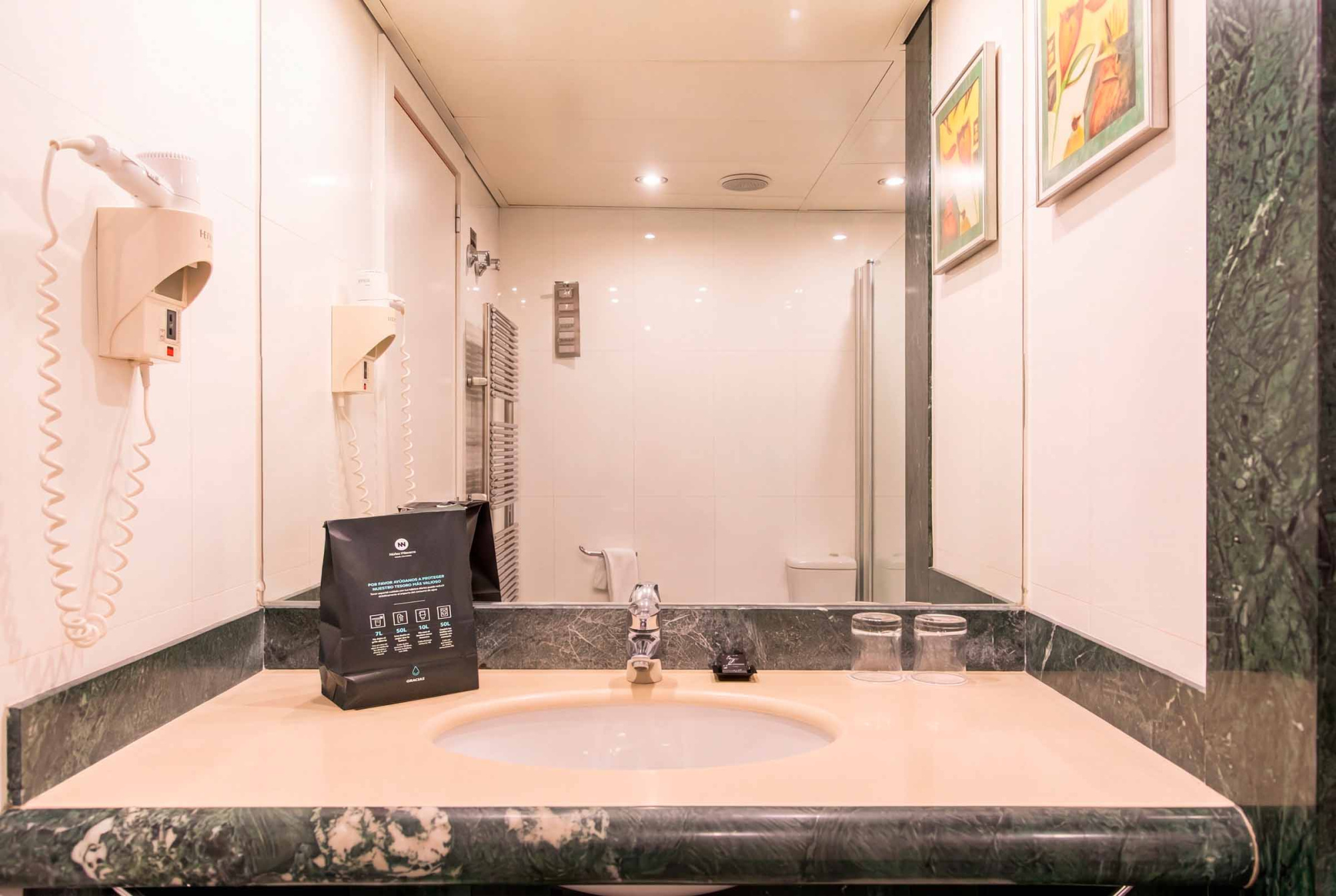 Se ve un lavabo empotrado con grifo y una zona de ducha con mampara en un baño iluminado.