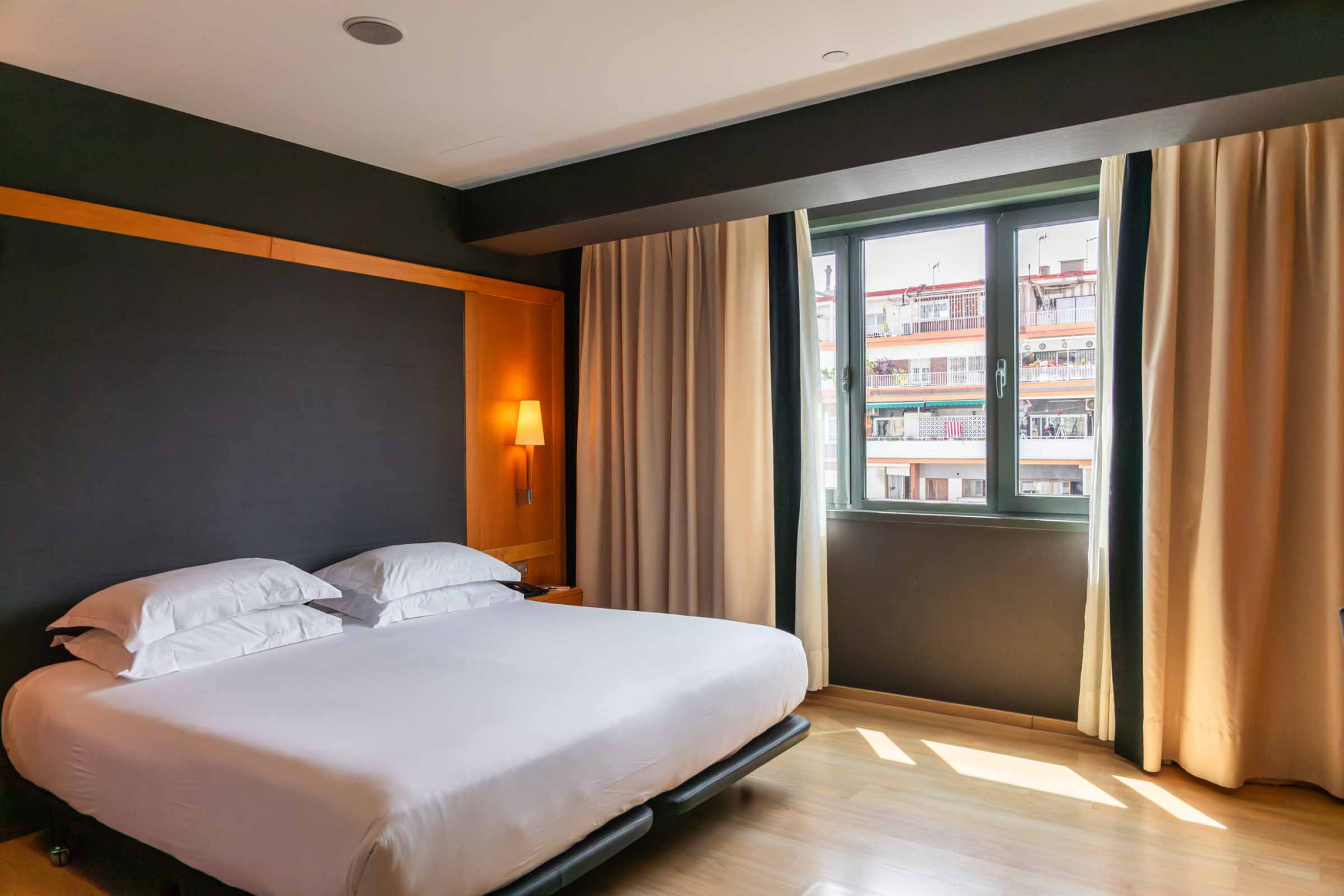 La habitación tiene una cama con ropa de cama blanca y un ventanal con cortinas beige.