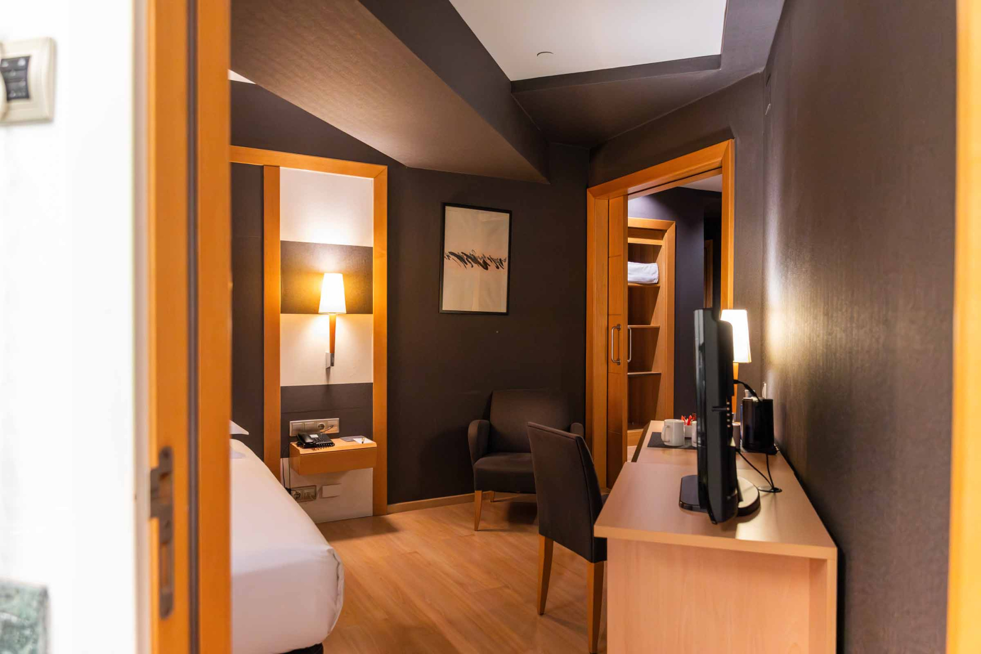 Se ve una habitación con cama doble, escritorio y lámpara junto a un pasillo interior.