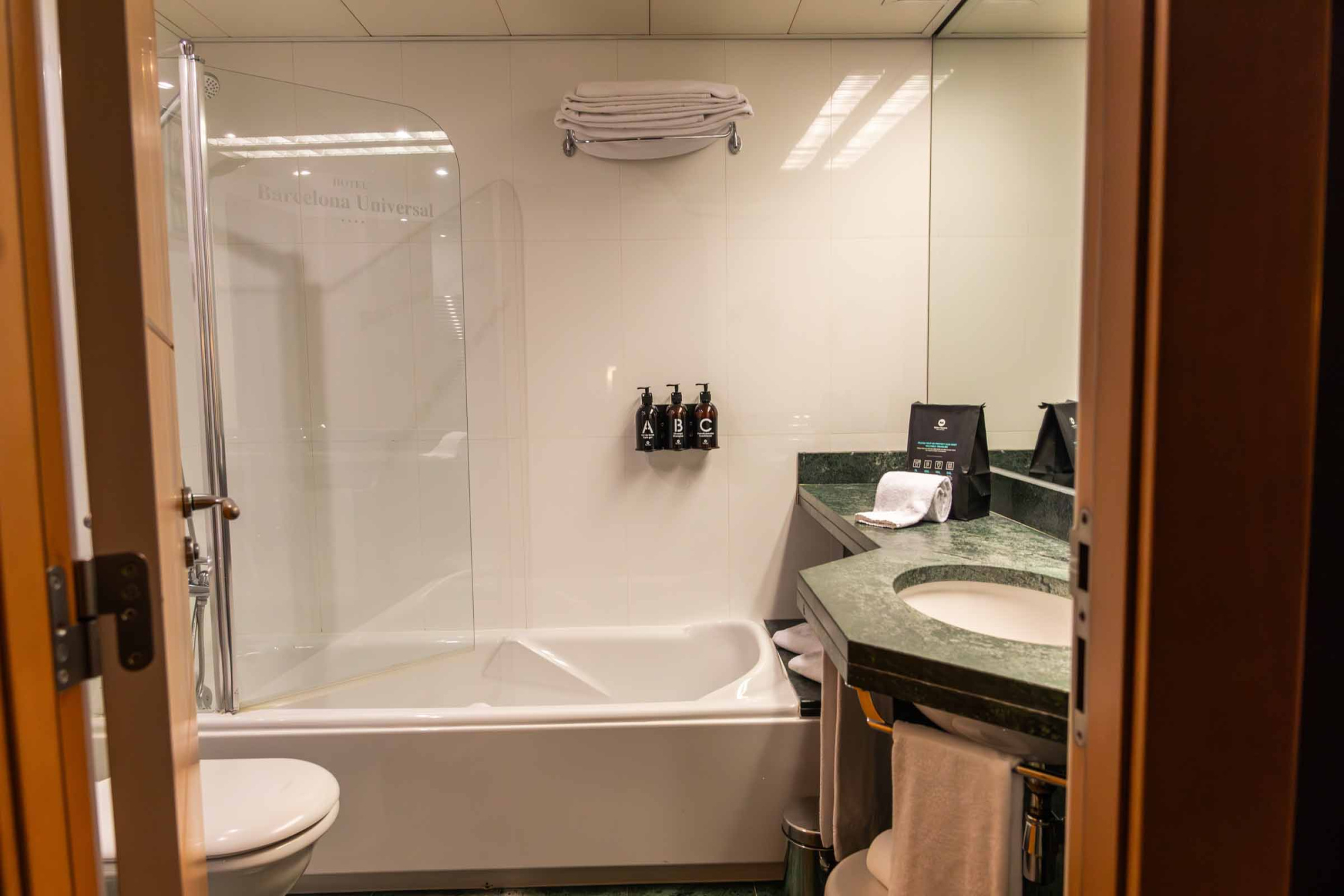 El baño muestra una bañera, un lavabo con encimera de piedra y una puerta abierta.