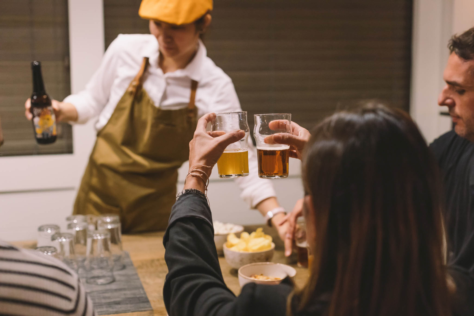 Un camarero sirve bebidas en vasos de cerveza mientras varios clientes conversan en un bar interior.