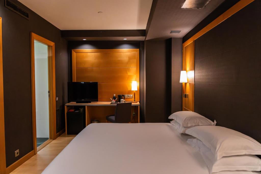 Una cama doble con mesitas y un escritorio con televisor iluminan el espacio interior