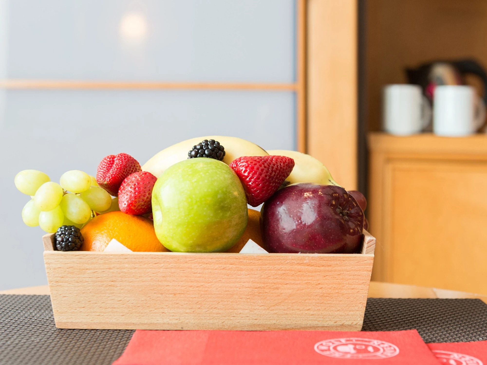 Una cesta de madera con frutas frescas sobre una mesa junto a una pared interior.