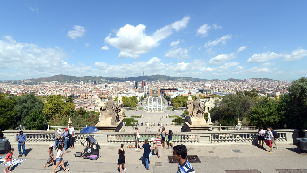 Personas pasean en un mirador de piedra con escaleras y la ciudad al fondo bajo un cielo despejado.