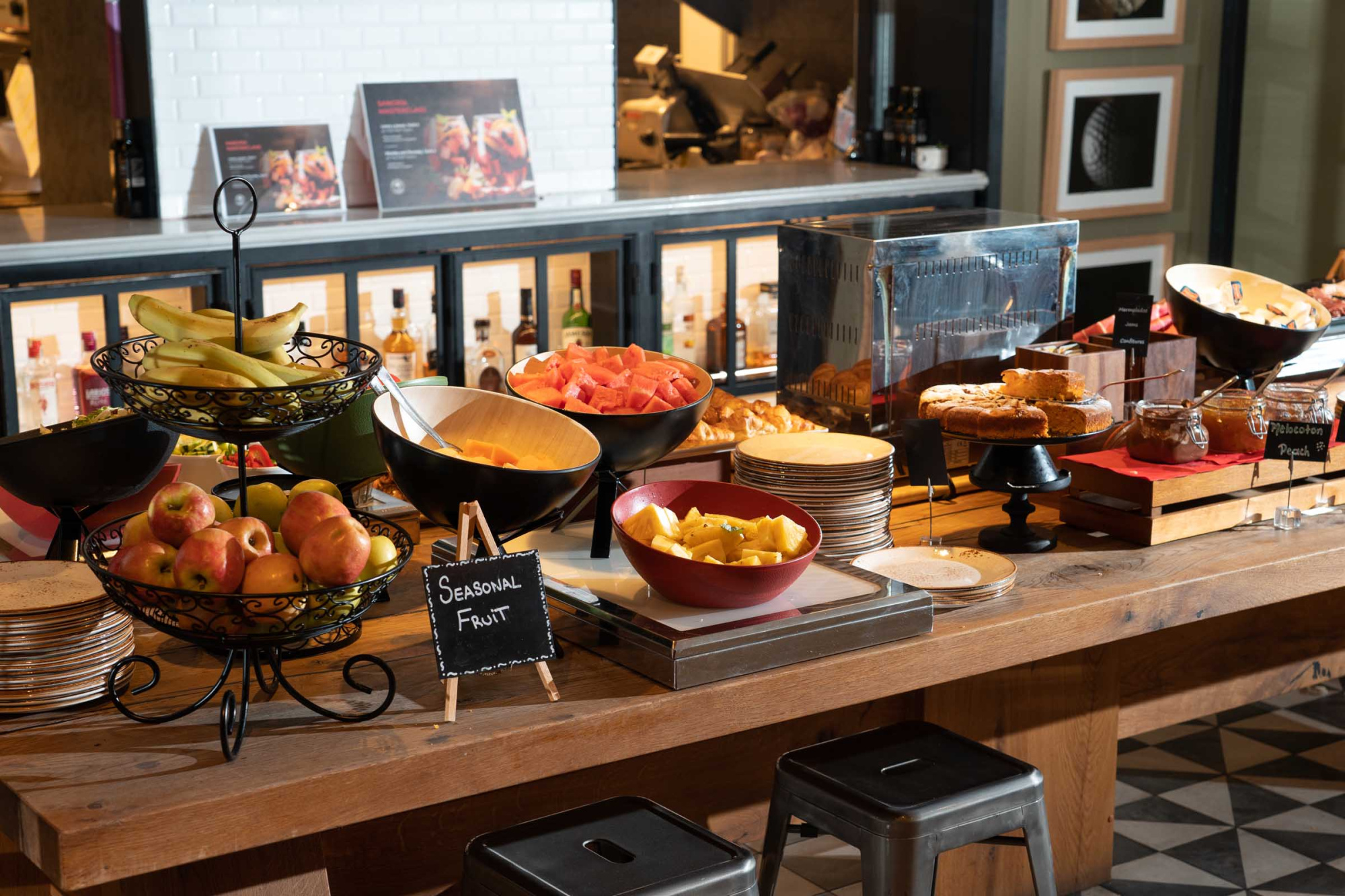 Se observa una mesa de buffet con bandejas metálicas y alimentos servidos en recipientes sobre un mostrador de madera.