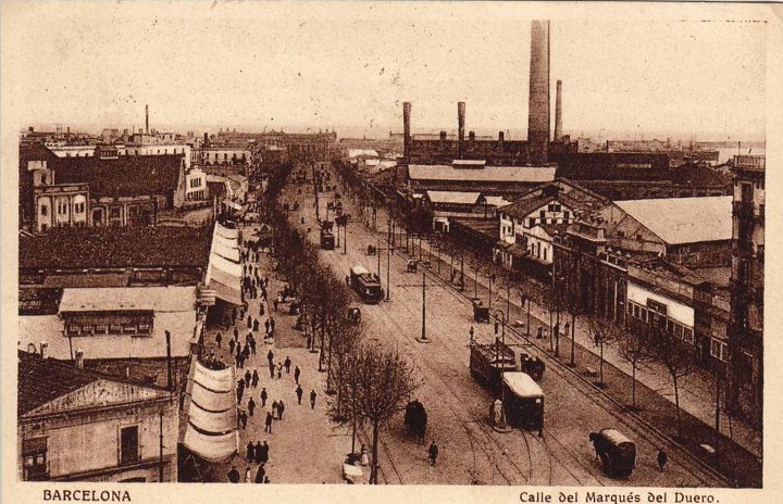 Vista antigua en blanco y negro de una calle con transeúntes, edificios y un puente elevado.